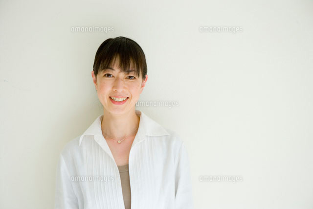 白い壁の前に立つ40代女性[30006001597A]｜ 写真素材・ストックフォト・画像・イラスト素材｜アマナイメージズ