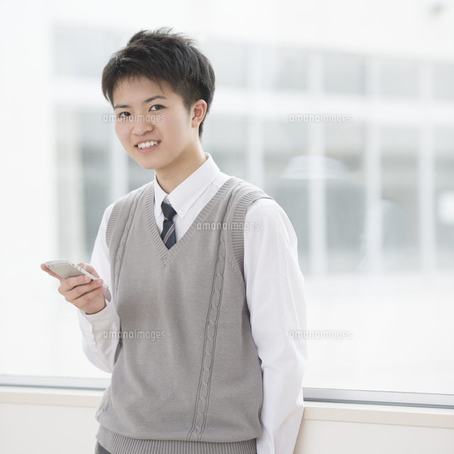 廊下でスマートフォンを持ち微笑む男子学生
(c)visual supple