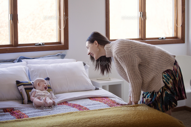 Side view of happy woman looking at cheerful baby girl lying on bed at home
(c)Cavan Images