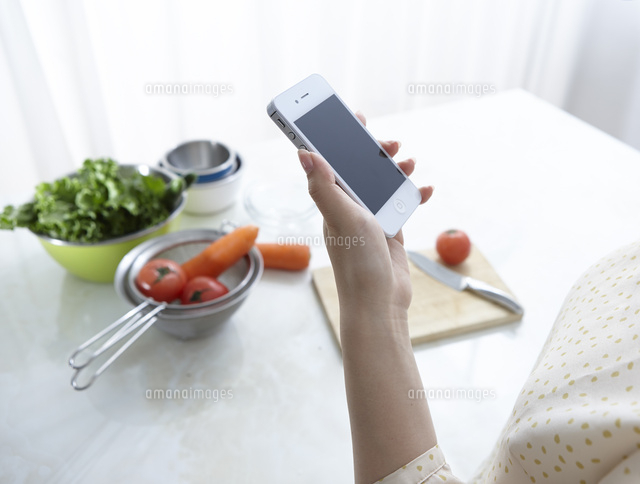 キッチンで携帯電話を持って料理の検索する女性の手
(c)Doable/a.collectionRF