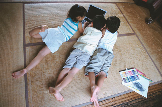 畳に寝そべりノートパソコンを見る日本人の3人の子ども
(c)absodels RF