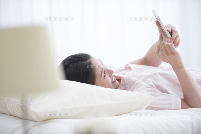 ベッドでスマホを見るパジャマの女性
(c)moonbase