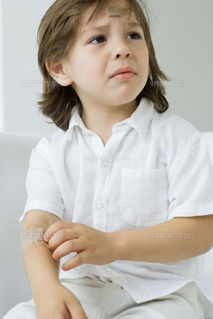 Little boy picking at adhesive bandage on his arm, frowning
(c)Odilon Dimier/PhotoAlto
