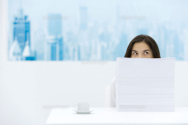 Woman sitting behind stack of paper, looking over and away
(c)Alix Minde/PhotoAlto