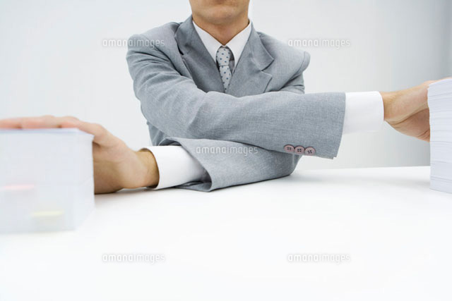 Man crossing his arms to put hands on top of stacks of paper
(c)Alix Minde/PhotoAlto