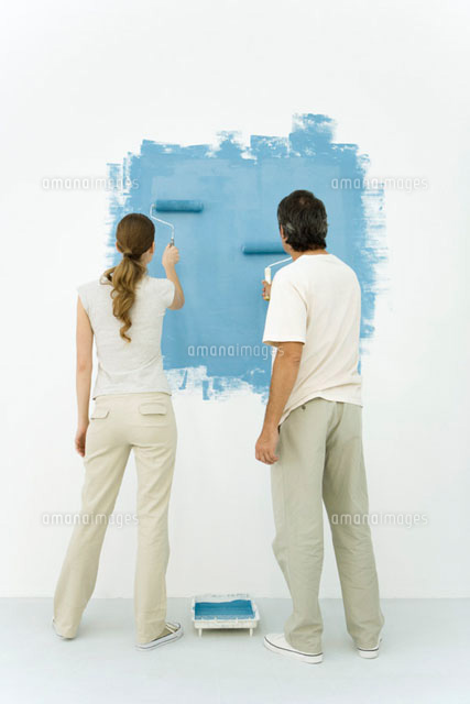 Couple painting wall blue using rollers, rear view
(c)Alix Minde/PhotoAlto