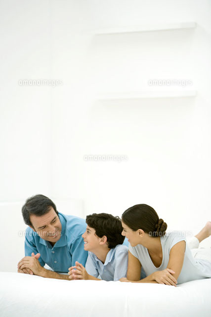 Family lying on bed together, smiling at each other
(c)Alix Minde/PhotoAlto