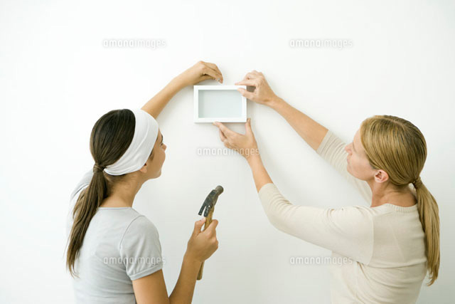 Mother and daughter attaching picture frame to wall
(c)Alix Minde/PhotoAlto