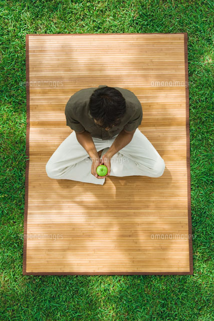 Man sitting indian style on mat outdoors,holding apple
(c)Odilon Dimier/PhotoAlto