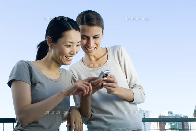 Two women looking at camera phone,smiling
(c)Michele Constantini/PhotoAlto