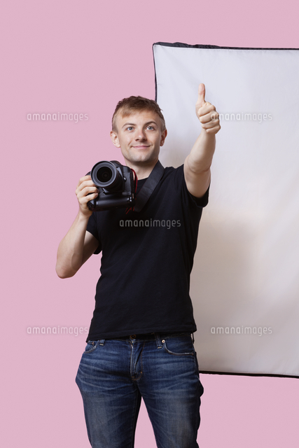 Happy photographer holding camera with thumbs up gesture over pink background
(c)moodboard