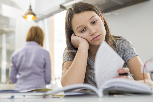 Bored girl studying at table with mother standing in background
(c)moodboard