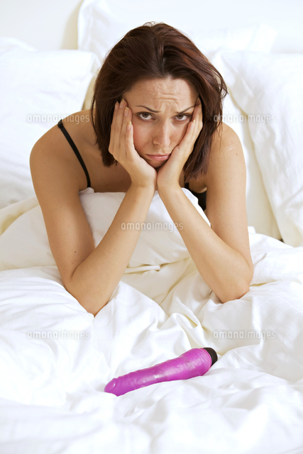 Portrait of young woman with hands on cheeks in front of dildo on bed
(c)moodboard