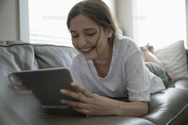 smiling tween girl using digital tablet on living room sofa
