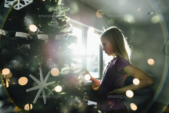 Side view of girl standing by illuminated Christmas tree at home
(c)Cavan Images