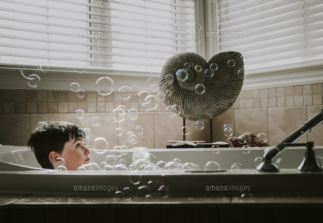 Boy looking at bubbles while taking bath in bathtub
(c)Cavan Images