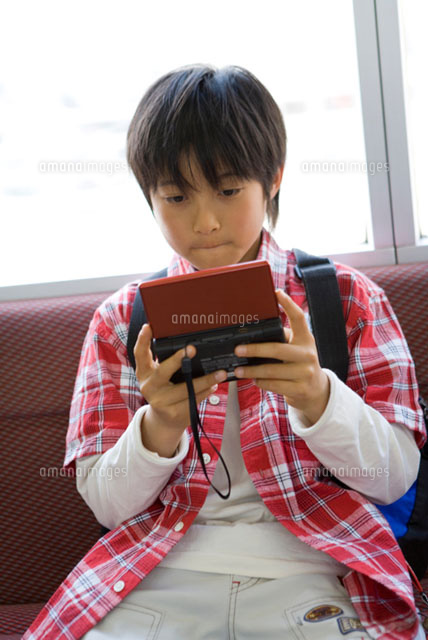 電車の座席に座ってゲームをする男の子
(c)DAJ