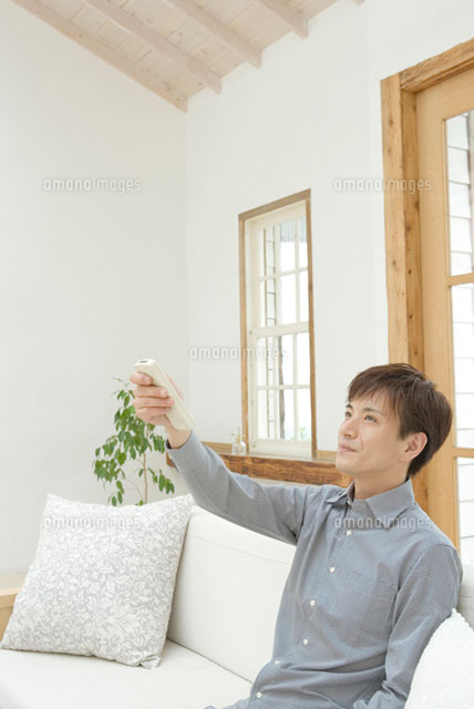 エアコンのリモコンを操作する男性
(c)DAJ
